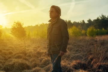 Man in green jacket and sunglasses in nature at sunrise during spring.