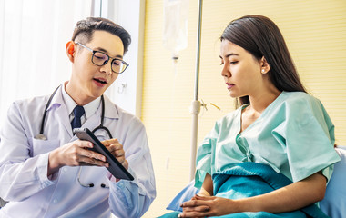 Asian male doctor talking to asian female patient in bed, while explaining exam results in computer to patient at medical consultation, Medicine and health care concept, selective focus point.