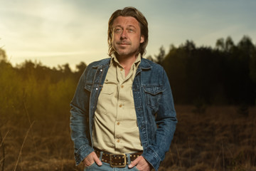 Naklejka na ściany i meble Man in denim jacket and shirt in nature reserve at sunrise during spring.