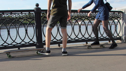 Fototapeta premium A guy teaches a girl to ride a skateboards without safety equipment near Embankment fence on a Sunny summer day, Moscow outdoor activity recreation, waist-high side view close up