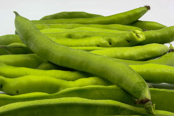 row of fresh green broad beans in their shells isolated on a white background