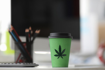 On table is a paper cup with lid painted hemp. Legalized stand-alone drink with hemp. Flavored...