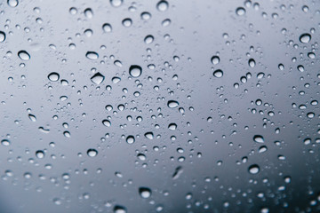 Close up of rain drops on the windshield, front window of a car on a blue gray background of dark sky.