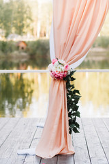 Wedding arch in the forest, in the fresh air, on the pier. Arch, decorated with beautiful fresh flowers and fabric. White, green & pink color. Wedding arch of real flowers.