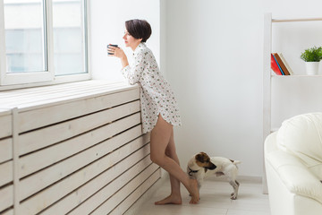Woman wearing cozy home shirt relaxing at home and playing with dog jack Russell terrier, drinking...