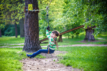 smiling boy rides a zip line. happy child on the zip line. The kid passes the rope obstacle course