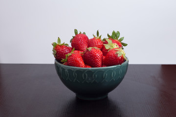 Green bowl full of strawberries on wooden table