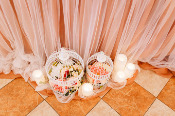 Wedding in the style vintage. Table decoration with cages, candles & candlestick. Elegant dining table in peach-pink color. Indoors wedding reception venue. Table with flowers, bottles, fruits, food.