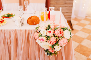 Wedding in the style vintage. Table decoration with cages, candles & candlestick. Elegant dining table in peach-pink color. Indoors wedding reception venue. Table with flowers, bottles, fruits, food.
