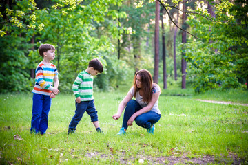 Fototapeta premium Young woman mother applying insect repellent to her two son before forest hike beautiful summer day or evening. Protecting children from biting insects at summer. Active leisure with kids