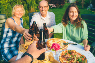 POV image of people toasting with beer bottles at multi generation family backyard party (focus on...