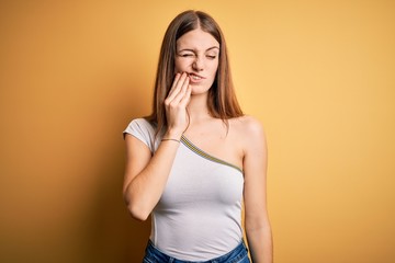 Young beautiful redhead woman wearing casual t-shirt over isolated yellow background touching mouth with hand with painful expression because of toothache or dental illness on teeth. Dentist