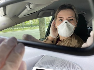 Fototapeta na wymiar girl in a protective mask looks in the mirror in a car. During quarantine- coronavirus. Covid-19.