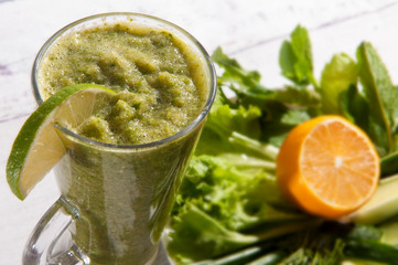 Healthy  smoothie detox from green salad, celery, cucumber, avocado,  mint, lime in long clear glass and plate of greens . Vegan