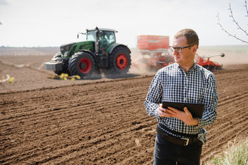 farmer in field examining sowing and holding tablet in his hands.