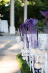 close up of purple ribbons on hooks with small hanging chandeliers on wedding ceremony aisle with white chairs