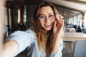 Image of happy woman in eyeglasses laughing and taking selfie photo - obrazy, fototapety, plakaty
