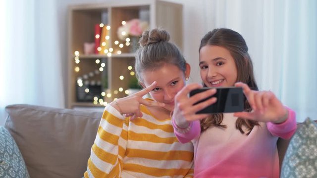people, technology and friendship concept - happy teenage girls taking selfie with smartphone sitting on sofa at home