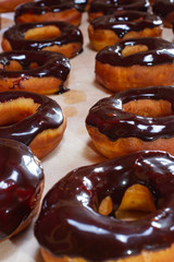 row of donuts coated with chocolate icing with a cup of black coffee