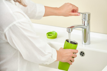 Woman dish washing a thermos bottle. Running water