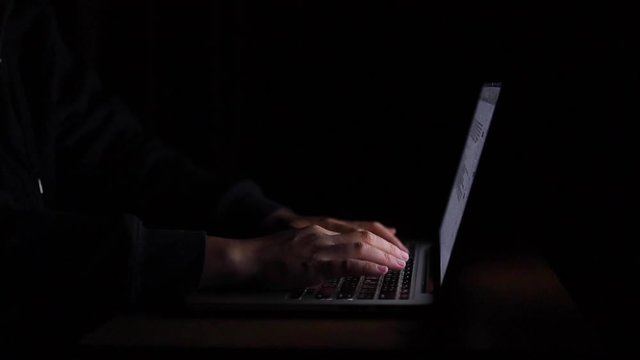 Hand of a man typing laptop computer for hacking or steal data at night in office. Hacking concept