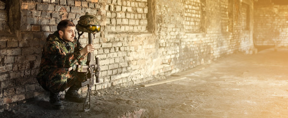 A male military soldier squatting took off his helmet and hung on the barrel of a machine gun