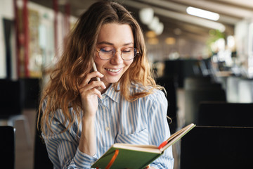 Image of cheerful young woman talking on cellphone and holding planner