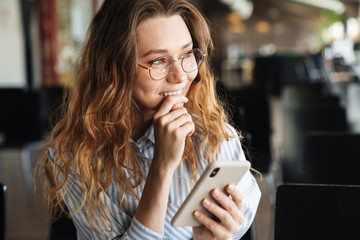 Image of cheerful young woman smiling and typing on cellphone
