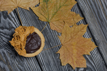Tartlets with chocolate ganache. On autumn maple leaves. Decorated with oil cream flowers. The cream has a caramel color. On brushed pine boards painted black.