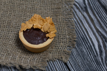 Tartlets with chocolate ganache. On a rough linen cloth. Decorated with oil cream flowers. The cream has a caramel color. On brushed pine boards painted black.
