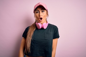 Young beautiful fitness sports woman wearing training cap and headphones over pink background afraid and shocked with surprise expression, fear and excited face.