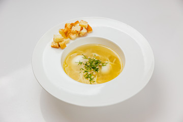 A white plate of soup with noodles, quail eggs and croutons