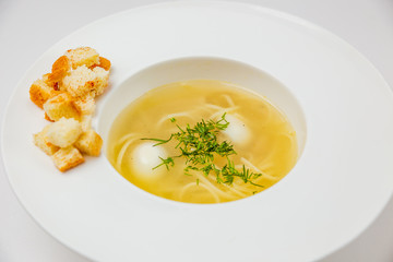 A white plate of soup with noodles, quail eggs and croutons