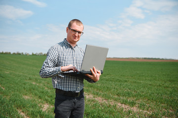 farmer standing in a wheat field and looking at laptop, are examining corp. Young handsome agronomist. Agribusiness concept. agricultural engineer standing in a wheat field