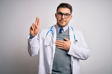 Young doctor man with blue eyes wearing medical coat and stethoscope over isolated background smiling swearing with hand on chest and fingers up, making a loyalty promise oath