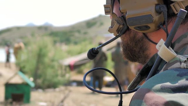 Airsoft. Soldier in headset talks. in a military camp