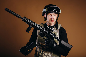Soldier with gun inserts magazine with cartridges on brown background. Concept of war. Veterans, comrades, soldiers. Man in uniform.