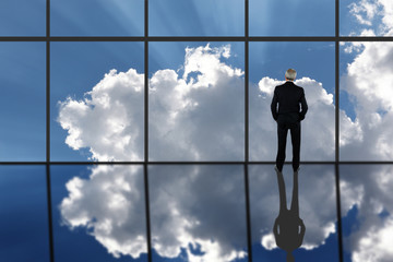 Businessman Standing in front of a large bank of windows with clouds and sun rays and reflection in the floor. Horizontal with copy space