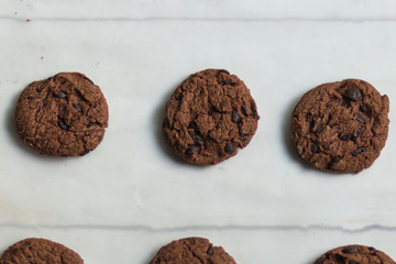 chocolate chip cookie on white cooking paper with wooden board flat lay top view close up