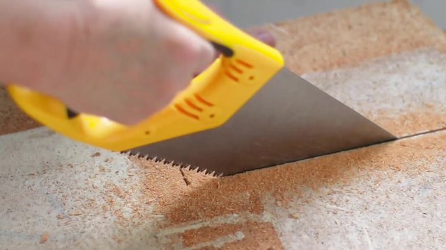 Close up of the human hand uses a handsaw and saws a wooden shield at home. A lot of sawdust from chipboard material. Construction concept