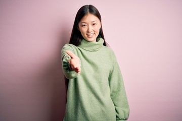 Young beautiful asian woman wearing green winter sweater over pink solated background smiling cheerful offering palm hand giving assistance and acceptance.