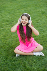 Schoolgirl enjoy melody. Listen music relaxing outdoors. Kid girl enjoy music green grass meadow. Pleasant time. Child headphones listen music. Girl headphones listening music. Modern technology