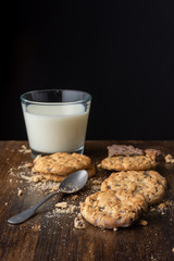 Close-up of chocolate chip cookies, crumbs, spoon and glass of milk, with selective focus, on wooden table and black background, with copy space