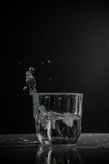 Transparent glass with splash of water on dark background