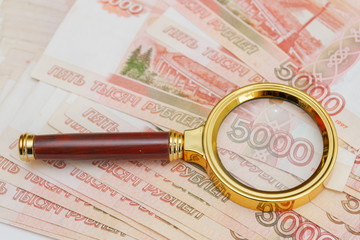 A magnifying glass with a gold handle is placed on top of Russian banknotes of five thousand rubles...