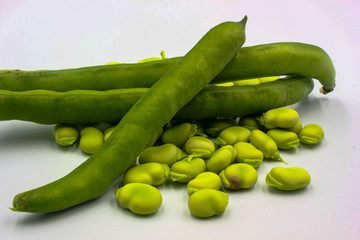 f open green broad beans in their shells and some shelled beans isolated on a white background