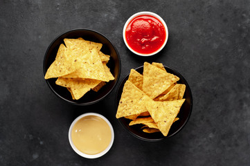 Two
bowls of mexican nachos chips and different sauces on a stone background with copy space for your text