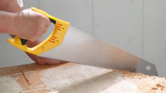 Human hand with a handsaw saws a chipboard in a house.