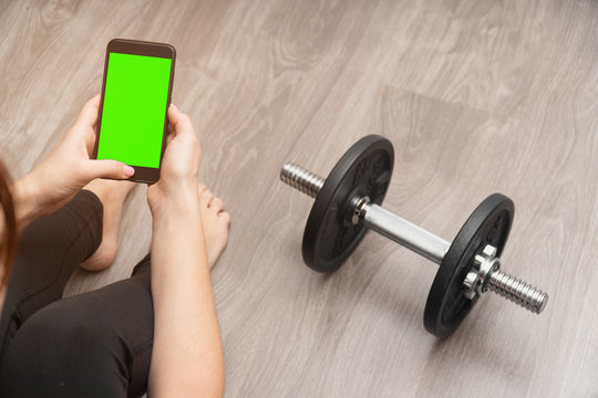 female hands holding smartphone with a green screen without an inscription, for playing sports online. Workout expectation concept