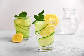 Concept 2 glasses with water and fresh slices of cucumber and lemon with mint on a light concrete background in a high key